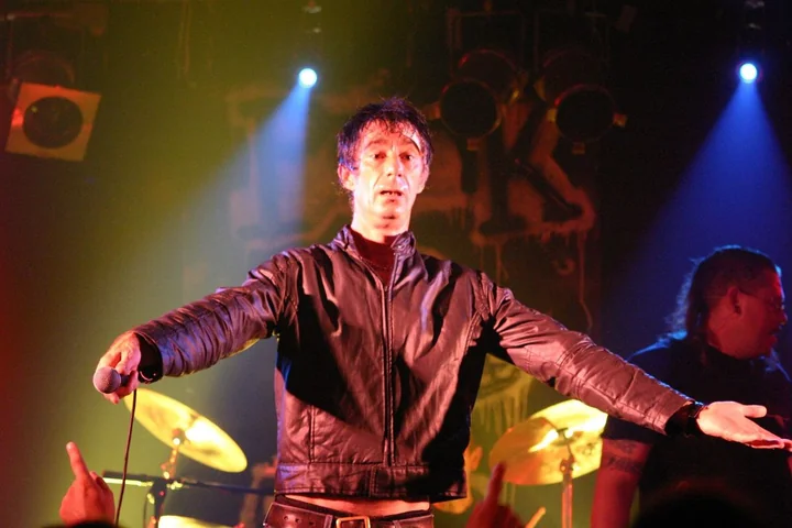 Jimmy Pursey performing live in a leather jacket, arms outstretched