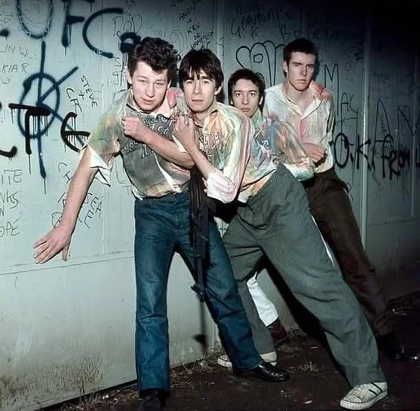 A punk band photographed against a graffiti-covered wall in the late 1970s
