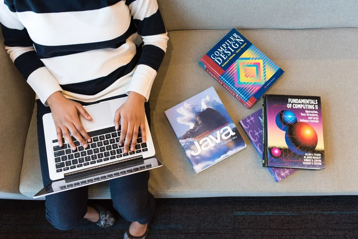 A person studying at a laptop surrounded by books