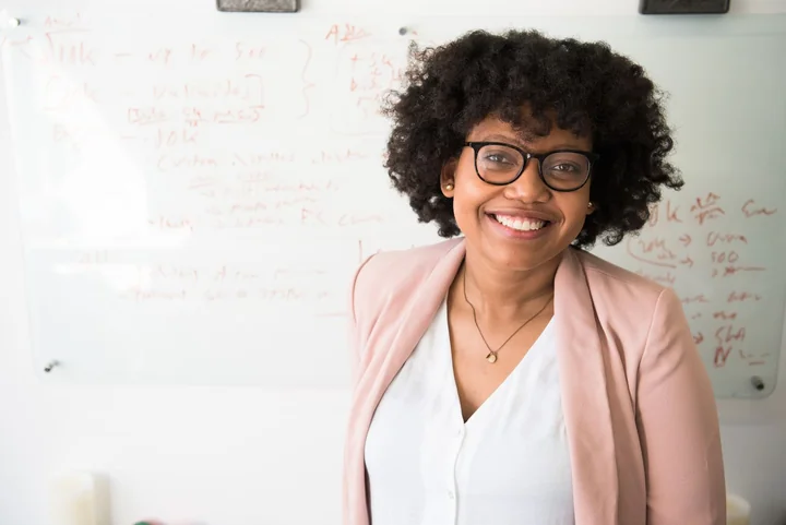 A woman in a blazer smiling beside a whiteboard