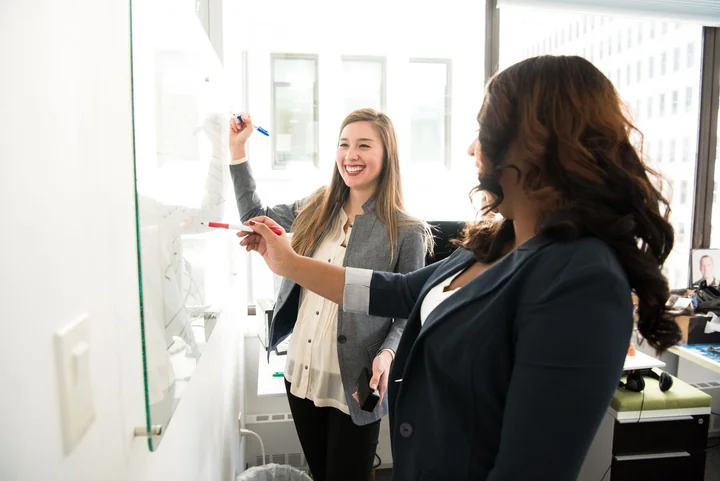 Two colleagues talking beside a glass whiteboard