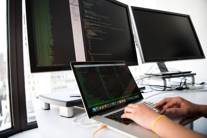 Hands typing at a desk with several monitors