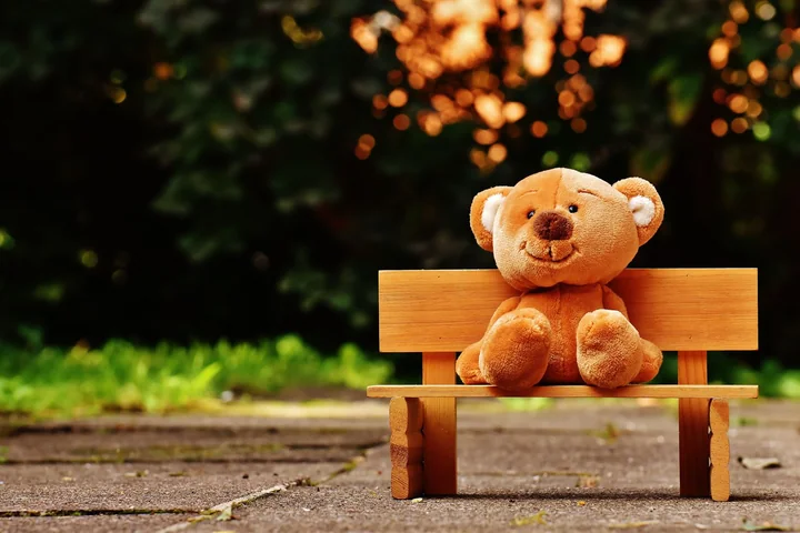 A teddy bear sitting on a wooden bench outdoors