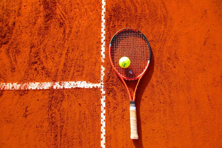 A tennis racket and ball on a clay court