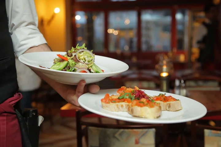 A waiter carrying two plated dishes in a restaurant