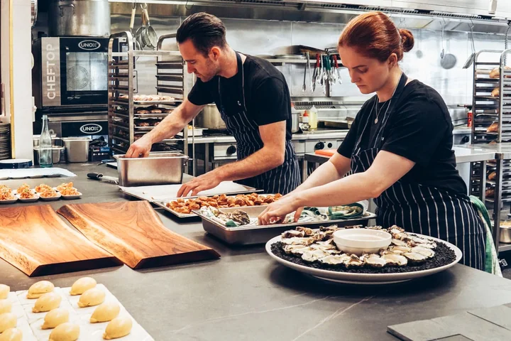 Two chefs preparing dishes side by side in a kitchen