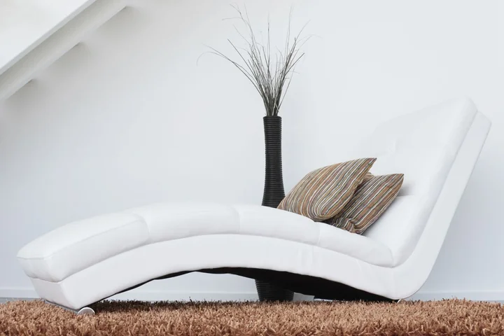 A white chaise longue beside a vase in a bright room