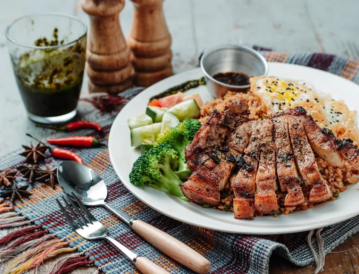 A plated meat dish with rice, salad and spices
