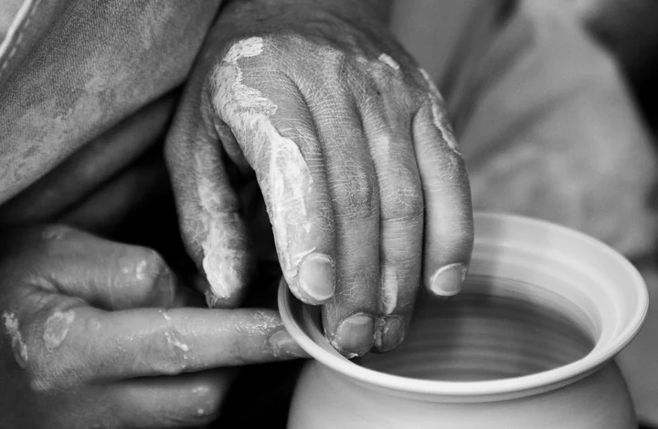 Hands shaping a bowl on a potter's wheel, in black and white