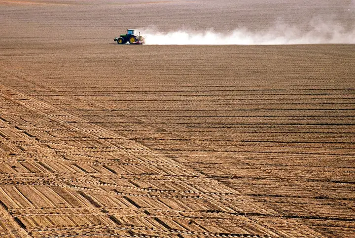 A tractor raising dust across a ploughed field