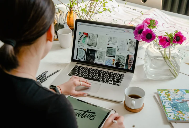 A woman working at a laptop beside flowers and a notebook