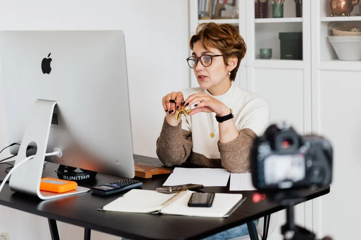 A woman being filmed at a desk by a camera