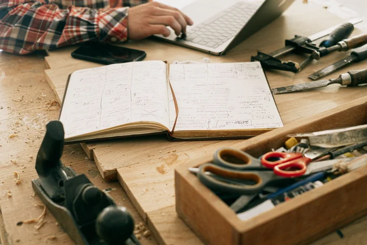 An open notebook and hand tools on a workbench