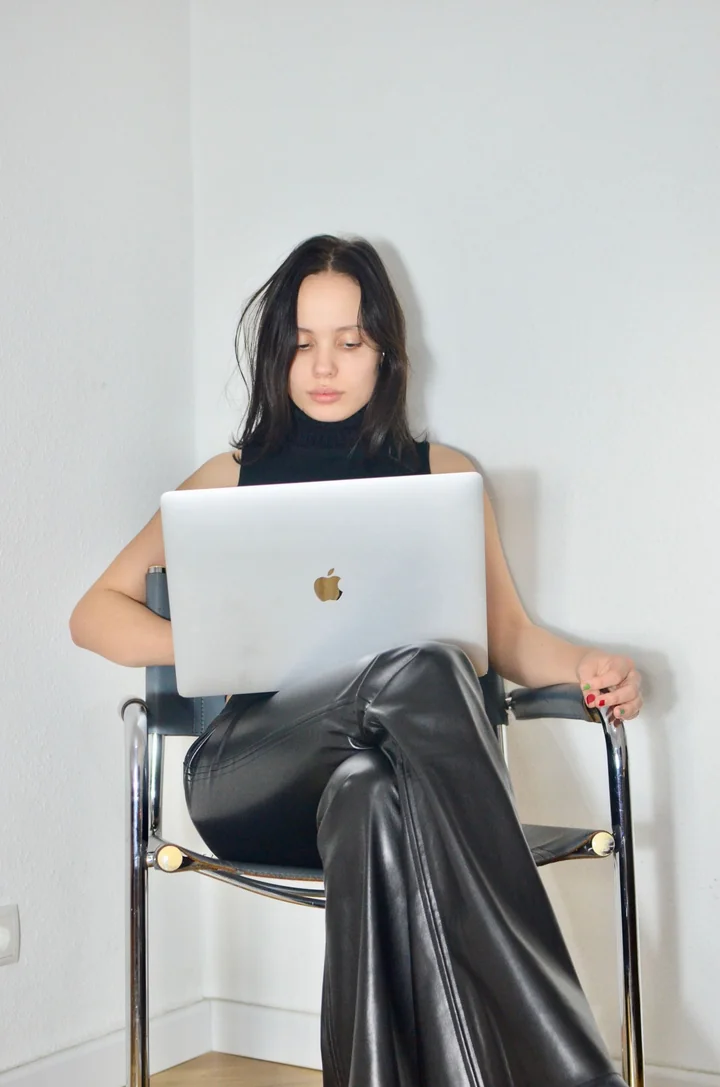 A woman sitting with a laptop on a plain background