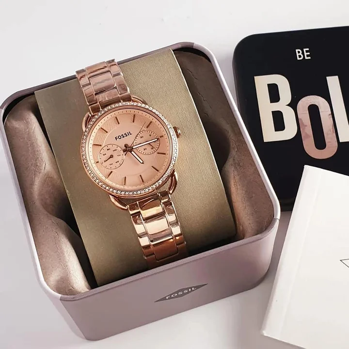 A gold wristwatch presented in a metal tin