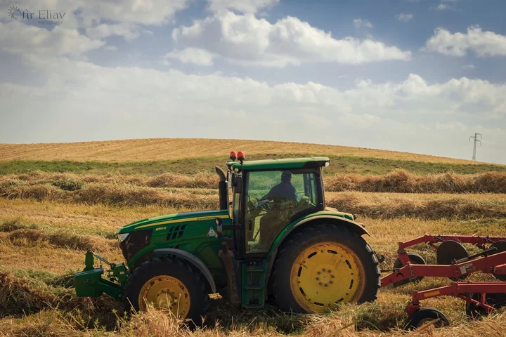 A green tractor in a field of cut straw